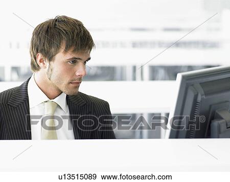 Stock Photo - Young Businessman at desk looking at computer. Fotosearch
