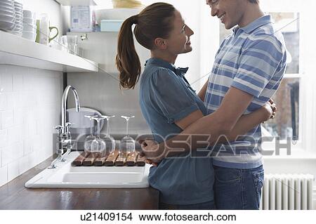 Picture - Young couple embracing in kitchen. Fotosearch