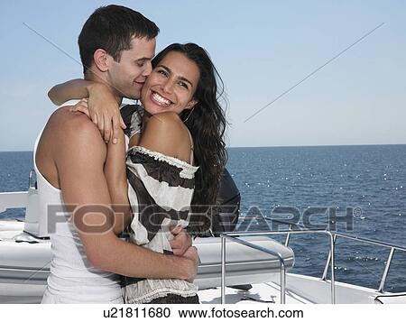 Stock Image - Young couple embracing on yacht, man kissing woman. Fotosearch