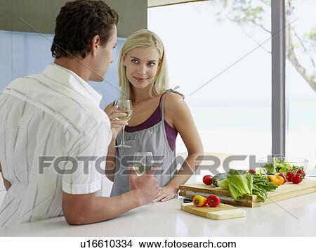 Picture - Young couple holding wineglasses, talking in kitchen. Fotosearch