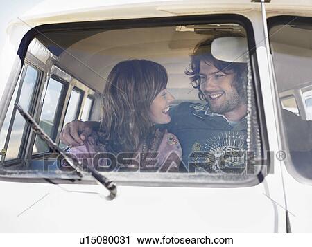 Stock Image - Young couple in camper van, smiling at each other, view through windscreen. Fotosearch