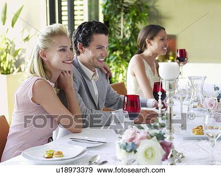 Young couple in formal clothing sitting side by side, arms around at table View Large Photo Image Stock Photo - Young couple in formal clothing sitting side by side, arms around at table. Fotosearch