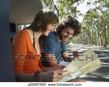 Stock Image - Young couple looking at map, sitting in open camper van at side of road. Fotosearch