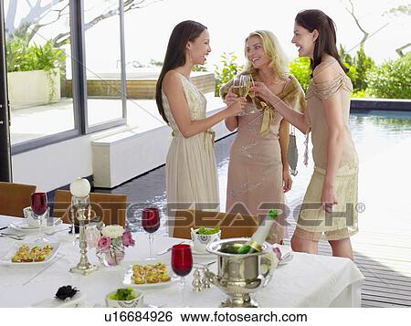 Stock Photograph - Young, female Friends drinking and socialising near pool at Dinner Party. Fotosearch