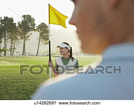 Young female golfer holding flag, defocused man in foreground View Large Photo Image Stock Photo - Young female golfer holding flag, defocused man in foreground. Fotosearch