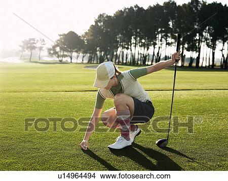 Young female golfer placing ball on tee View Large Photo Image Picture - Young female golfer placing ball on tee. Fotosearch