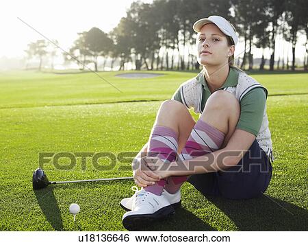 Stock Photograph - Young female golfer sitting on court, portrait. Fotosearch