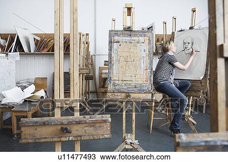 Stock Image - Young female student drawing with charcoal in college art studio. Fotosearch