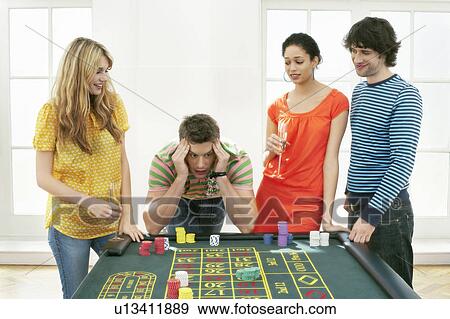 Stock Photo - Young frustrated man at roulette table with friends. Fotosearch