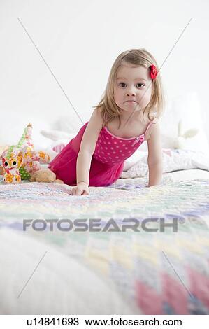 Stock Image - Young girl, 2-3 years crawling on bed. Fotosearch