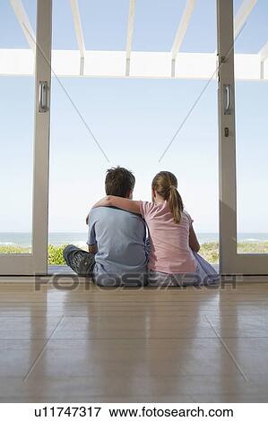 Stock Photo - Young girl and boy sitting on floor in doorway, back view. Fotosearch