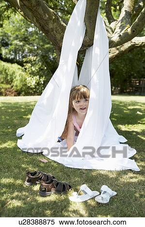 Stock Photography - Young girl in back yard peeking out of tent made of sheet. Fotosearch