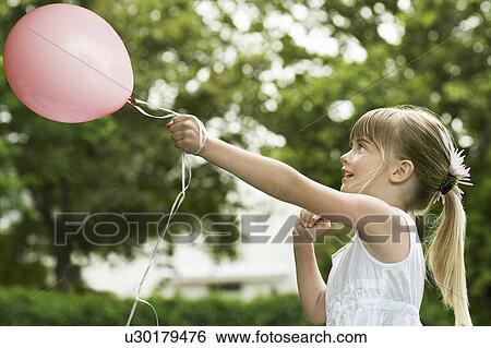 Stock Photograph - Young girl playing with pink balloon, side view. Fotosearch