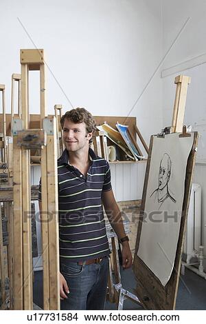 Young male artist standing by charcoal portrait in studio View Large Photo Image Picture - Young male artist standing by charcoal portrait in studio. Fotosearch