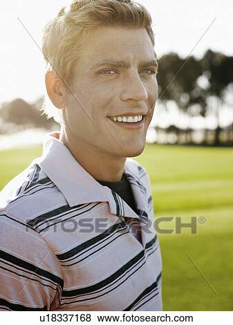 Stock Photo - Young male golfer on court, smiling. Fotosearch