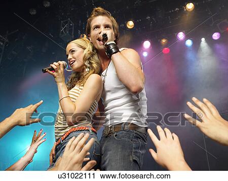 Young man and woman singing on stage in concert in front of adoring fans, low angle view View Large Photo Image Stock Image - Young man and woman singing on stage in concert in front of adoring fans, low angle view. Fotosearch