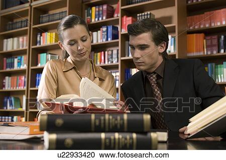 Stock Image - Young man and woman studying at desk in library. Fotosearch
