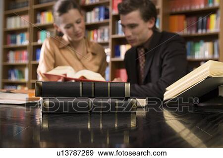 Young man and woman studying at desk in library, focus on books in foreground View Large Photo Image Stock Photo - Young man and woman studying at desk in library, focus on books in foreground. Fotosearch