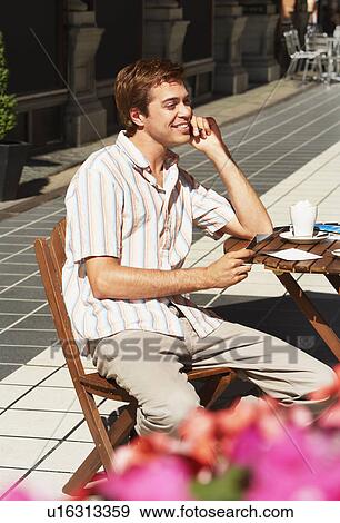 Stock Photo - Young Man at Outdoor Cafe holding postcard. Fotosearch