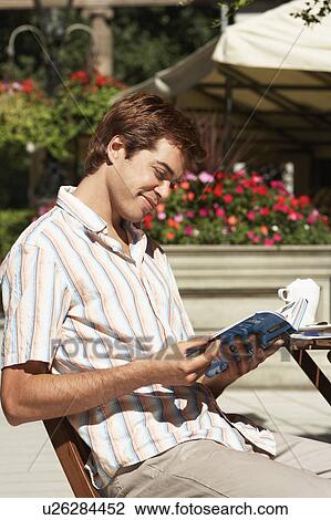 Stock Image - Young Man at Outdoor Cafe reading guidebook. Fotosearch