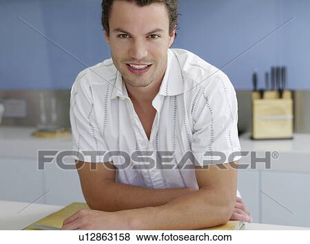 Young man leaning on kitchen counter on cutting board View Large Photo Image Stock Photo - Young man leaning on kitchen counter on cutting board. Fotosearch