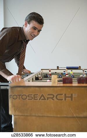 Stock Photograph - Young man playing table football in game room. Fotosearch