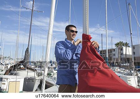 Picture - Young man securing sail of boat. Fotosearch