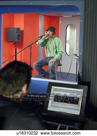 Stock Image - Young man singing in studio, technician in foreground. Fotosearch