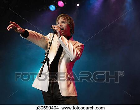 Young Man Singing into microphone on stage at Concert, low angle view View Large Photo Image Picture - Young Man Singing into microphone on stage at Concert, low angle view. Fotosearch