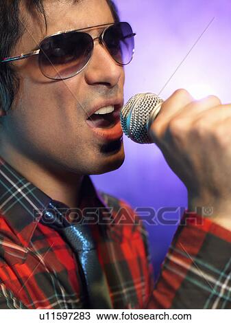 Stock Image - Young Man Singing into microphone on stage at Concert, close up. Fotosearch