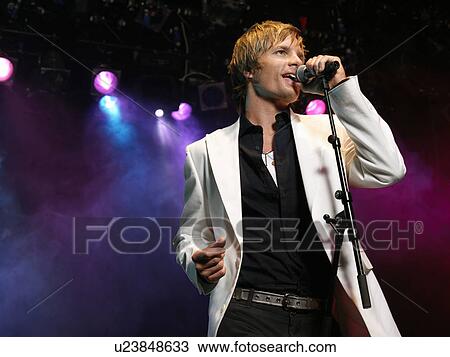 Stock Image - Young Man Singing into microphone on stage at Concert, low angle view. Fotosearch
