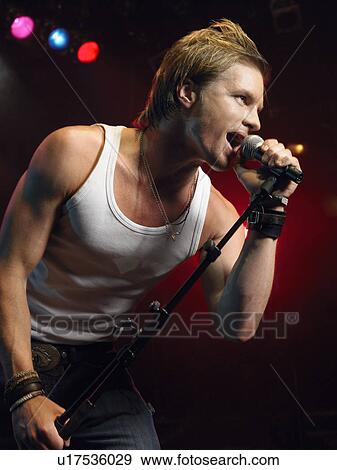 Stock Photo - Young Man Singing into microphone on stage at Concert, low angle view. Fotosearch