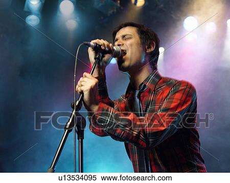 Stock Photography - Young Man Singing into microphone on stage at Concert, low angle view. Fotosearch