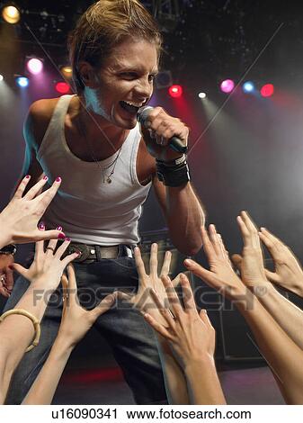 Stock Image - Young Man Singing on stage in concert close to adoring fans, low angle view. Fotosearch