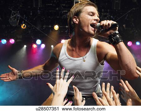 Stock Image - Young Man Singing on stage in concert close to adoring fans, low angle view. Fotosearch