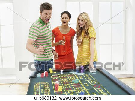 Stock Image - Young man with friends celebrating gambling win at roulette table. Fotosearch