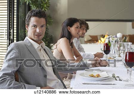 Young, stylishly dressed man sitting at table of formal dinner party, smiling View Large Photo Image Stock Photograph - Young, stylishly dressed man sitting at table of formal dinner party, smiling. Fotosearch