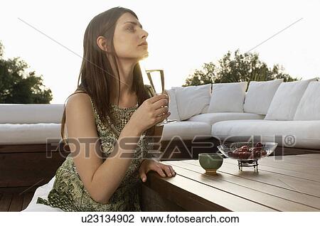 Stock Image - Young woman drinking champagne and eating fruit, portrait. Fotosearch