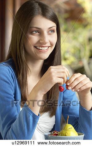 Stock Image - Young woman eating fruit, portrait. Fotosearch