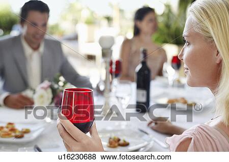 Young woman holding wineglass, sitting at table with friends View Large Photo Image Stock Photo - Young woman holding wineglass, sitting at table with friends. Fotosearch