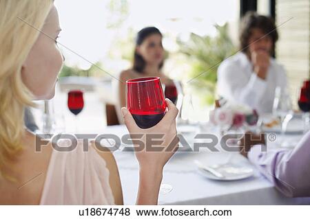 Young woman holding wineglass, sitting at table with friends, back view View Large Photo Image Stock Photo - Young woman holding wineglass, sitting at table with friends, back view. Fotosearch