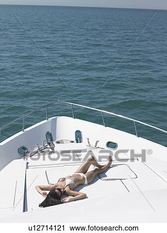 Stock Image - Young woman in bikini sunbathing on yacht, elevated view. Fotosearch