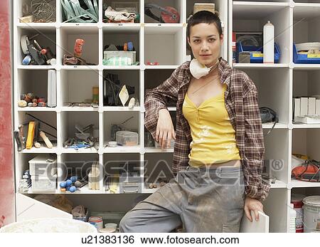 Stock Photograph - Young Woman leaning on Tool Shelves, portrait. Fotosearch