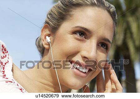 Stock Photo - Young woman listening to music through earphones, portrait. Fotosearch