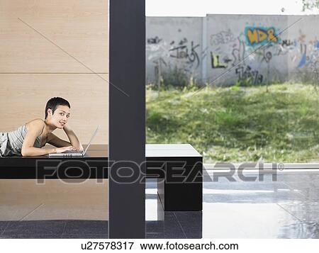 Young woman lying down using laptop indoors, portrait View Large Photo Image Stock Photo - Young woman lying down using laptop indoors, portrait. Fotosearch