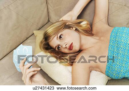 Stock Image - Young woman lying on sofa playing cards, high angle view, close up. Fotosearch