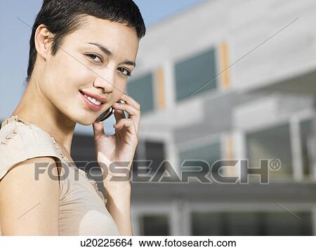 Picture - Young woman on cell phone standing in plaza. Fotosearch