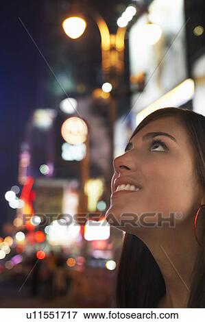 Stock Photo - Young Woman on Sidewalk at Night, Looking Up. Fotosearch
