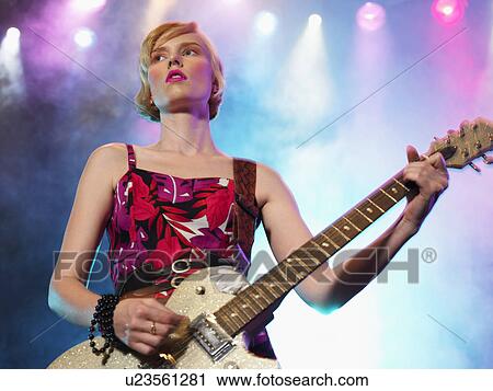 Stock Image - Young Woman playing guitar in concert on stage, low angle view. Fotosearch