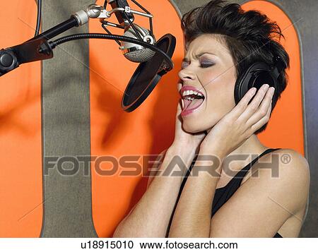 Stock Image - Young woman singing in studio, portrait. Fotosearch